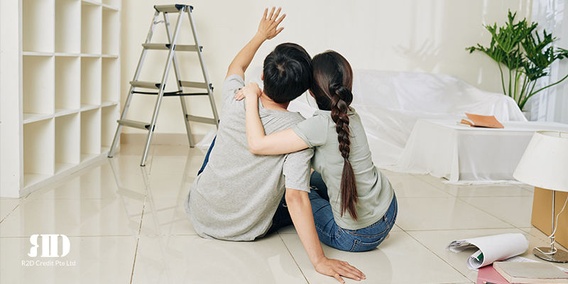 Back view of a couple sitting on the floor in a new house and pointing to the wall to indicate renovation