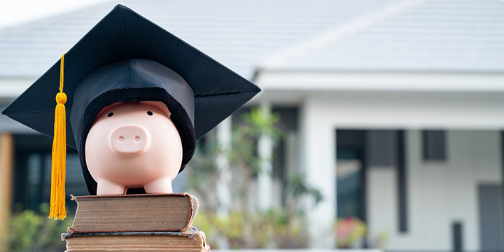 Piggy bank with a graduation cap on it with the background of a college steps to indicate an education loan