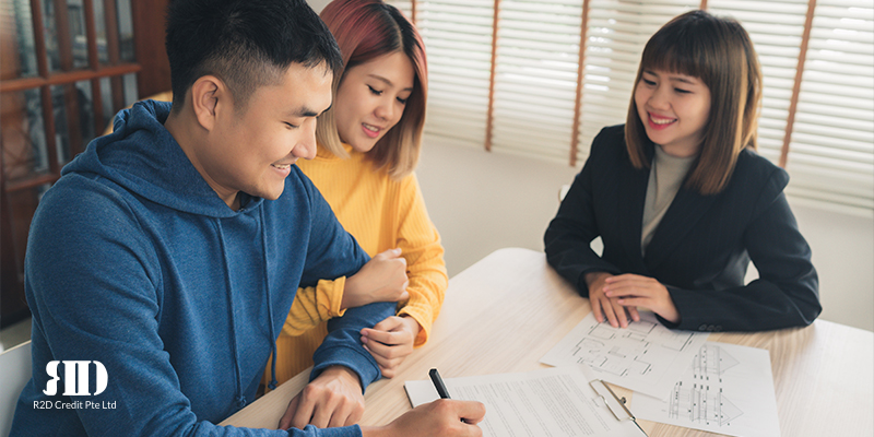  Young couple smiling as they sign a bridging loan document as agent looks on, with a smile 