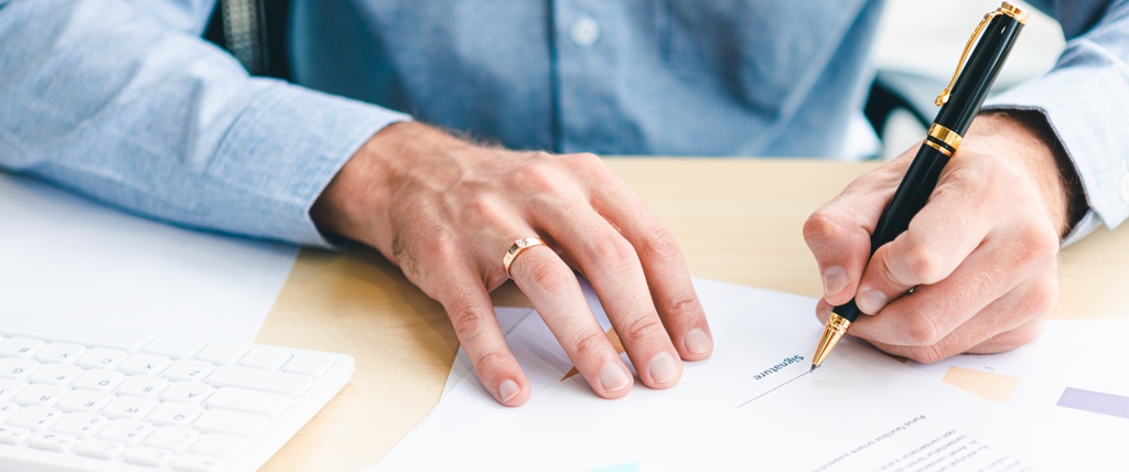 Close-up of male hand signing a personal loan document placed upon a brown table