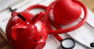 Red piggybank on a desk beside a red stethoscope
