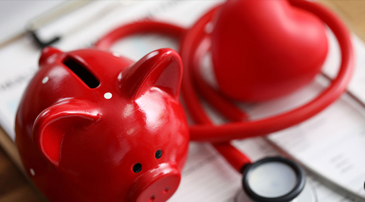 Red piggy bank on a desk beside a red stethoscope to indicate a medical loan