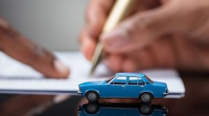 Blue model car on a desk as a man shows another man where to sign on a contract for a Grab loan
