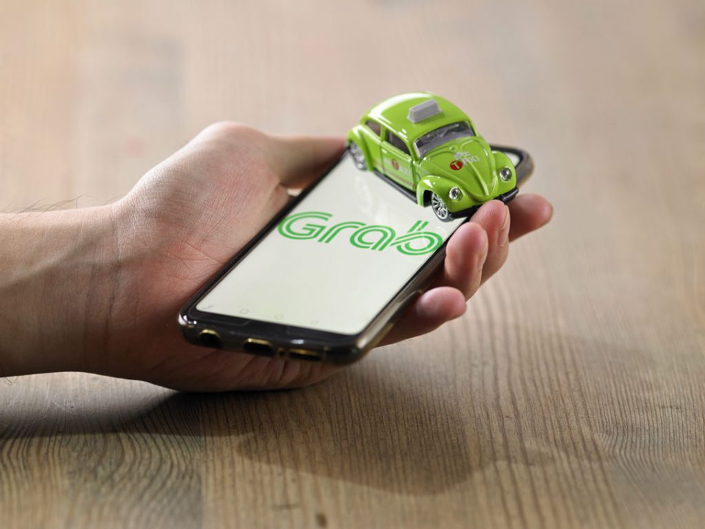 Man holding a mobile phone with Grab app on and toy cab placed on the phone, representing the need for Grab finance.