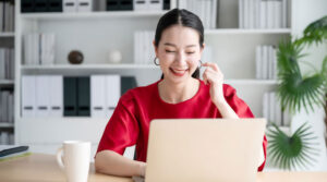 Smiling Asian woman looking at a laptop with a coffee mug on the table next to her to indicate a loan approval from a licensed money lender in Singapore