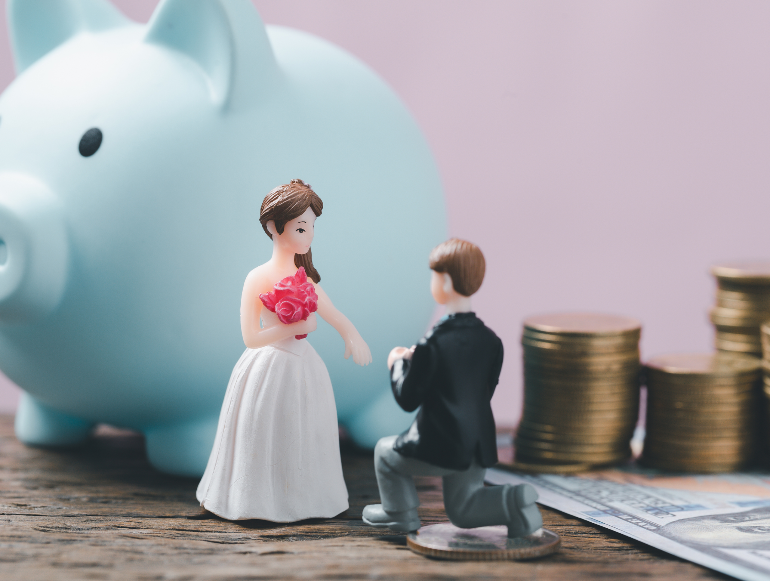 A mini figurine of a wedded couple beside a row of stacked coins in ascending order, representing the costs of a wedding